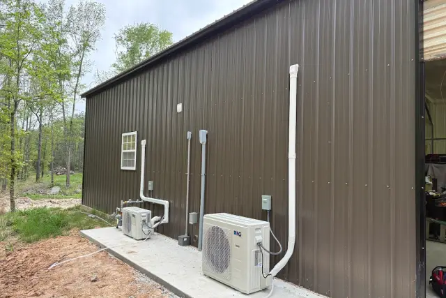 Two ductless mini split condensers mounted on a concrete pad beside a metal barndominium, each serving a separate zone inside the building
