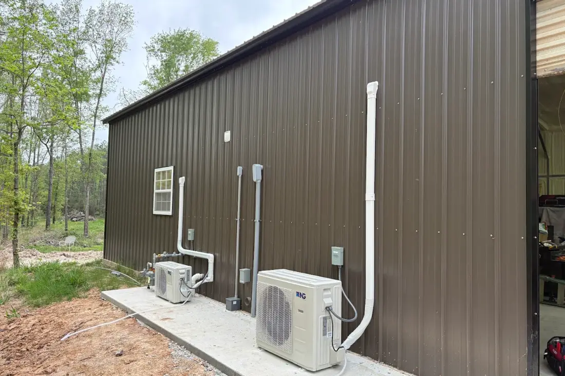 Two ductless mini split condensers mounted on a concrete pad beside a metal barndominium, each serving a separate zone inside the building