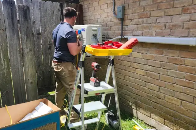 A licensed installer using manifold gauges, a vacuum pump, and power tools to commission a ductless mini split at a Texas home