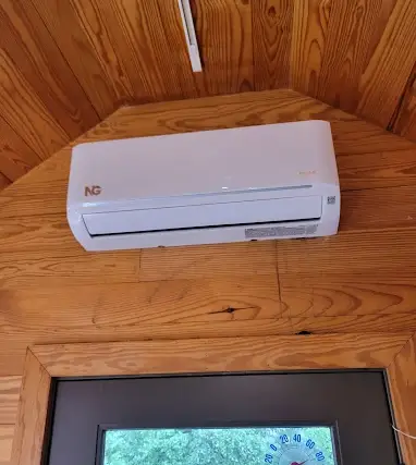 A clean wall-mounted ductless mini split indoor head on a wood-panelled interior wall