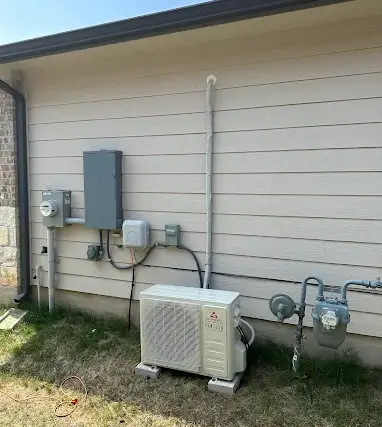A mini split condenser installed beside a home electrical panel, disconnect switch, and utility meters